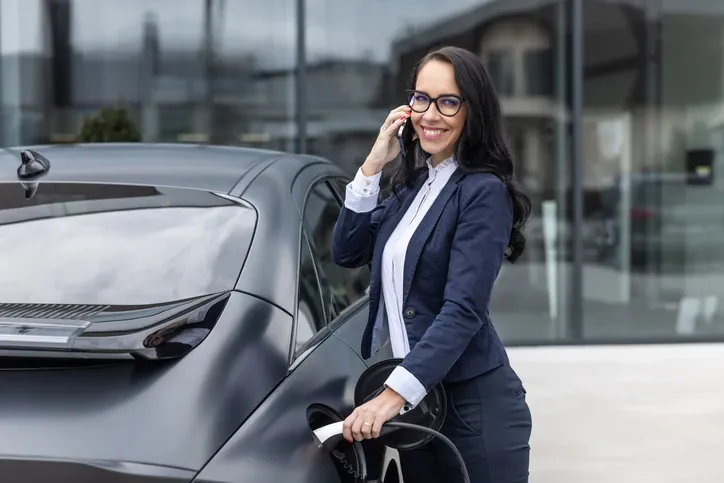 Kobieta podłączająca samochód hybrydowy typu plug-in do ładowania, wykorzystując publiczną ładowarkę.